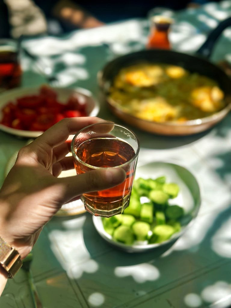A refreshing beverage enjoyed outdoors during a sunlit meal with fresh vegetables.