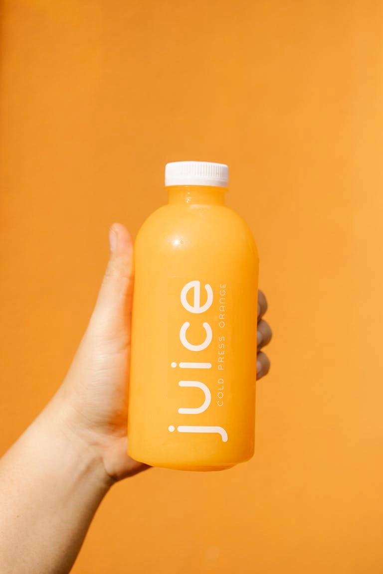 Bright orange juice bottle in hand against an orange background, symbolizing fresh and healthy living.