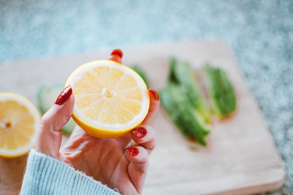 Close-up of a hand with red nails holding a fresh sliced lemon, perfect for culinary or health-themed projects.