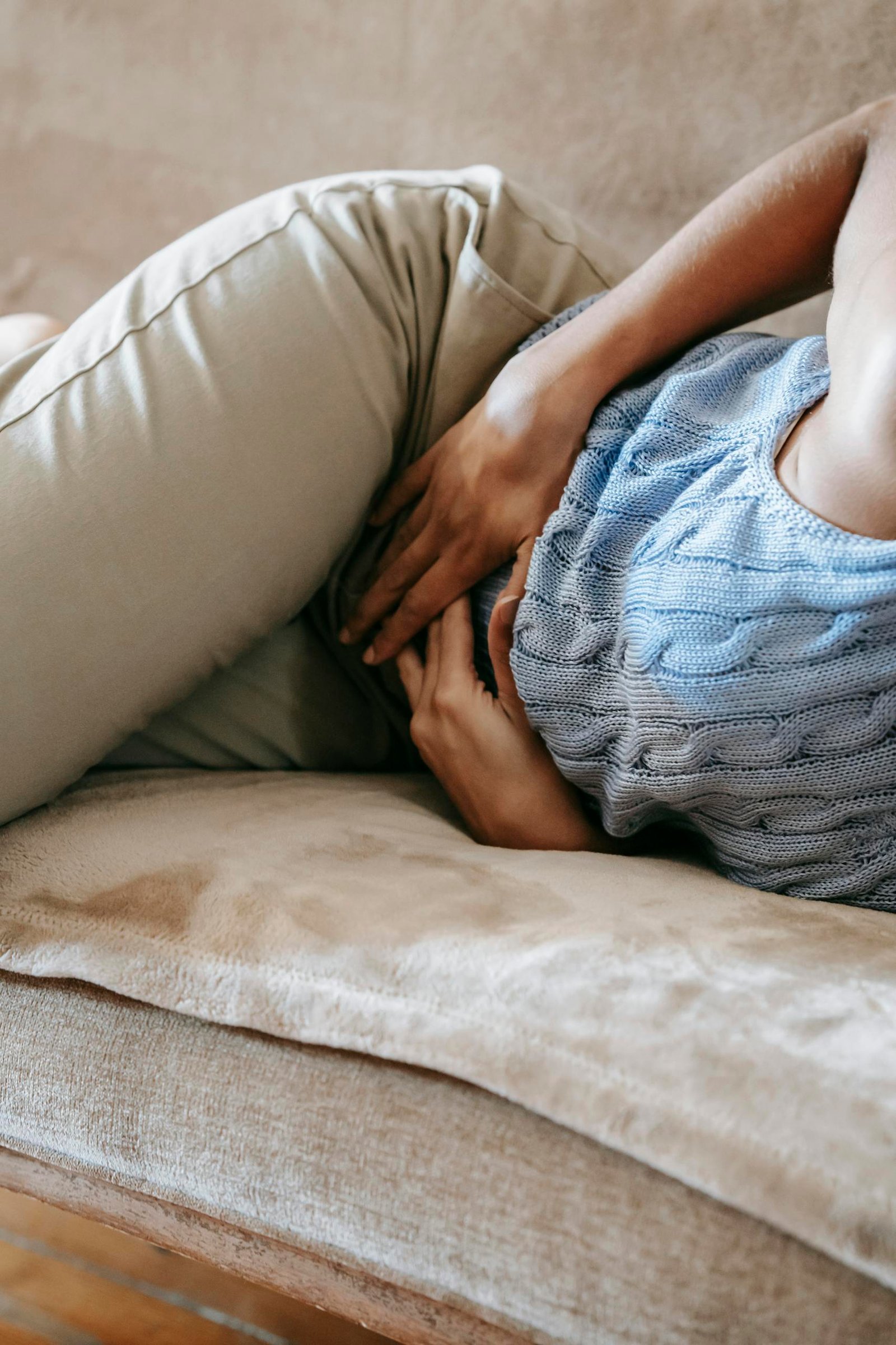 Crop anonymous female in casual outfit writhing on sofa while having stomach ache