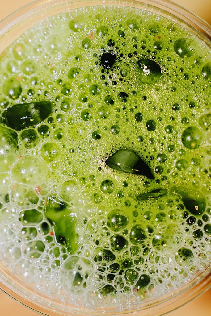 Top view of a refreshing green juice with visible foam and leaves, showcasing a healthy beverage.