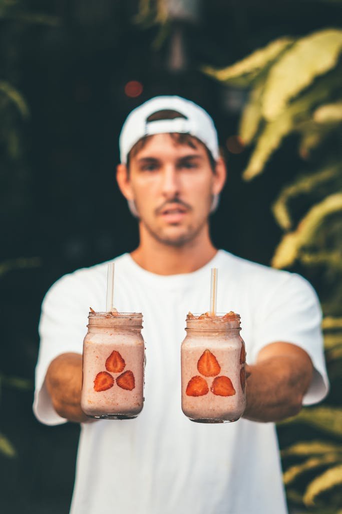 Young man offers refreshing strawberry smoothies outdoors in Bali. Perfect for summer lifestyle.